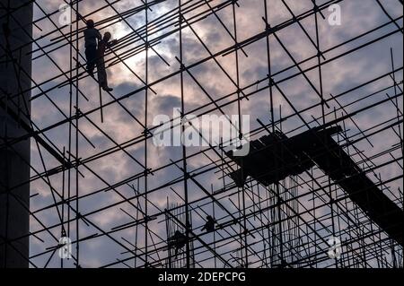 Silhouette von Arbeitern hoch auf Gerüsten auf einer Baustelle, mit Schutzhüten, aber keine andere Sicherheitsausrüstung oder persönliche Schutzausrüstung. Stockfoto