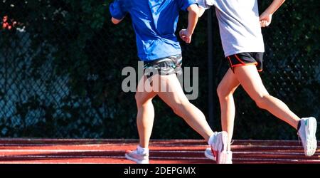 Seiten- und Rückansicht von zwei High School Girls, die beim Training auf einer Strecke in Shorts schnell miteinander laufen. Stockfoto