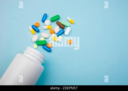 Mehrfarbige Tabletten und Kapseln, weiße Flasche für Tabletten, pharmazeutische Medikamente Pillen auf blauem Hintergrund, Analgetikum gegen Krankheiten Stockfoto