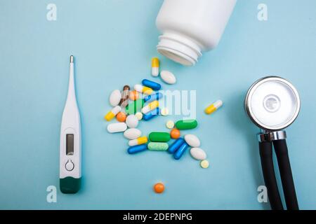 Mehrfarbige Tabletten und Kapseln, ein Thermometer und ein Tonometer auf blauem Hintergrund, Konzept der Behandlung für einen kranken Menschen Stockfoto