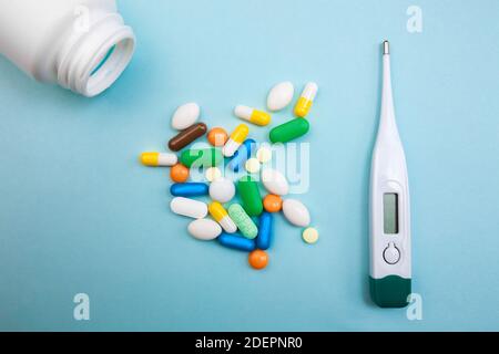 Mehrfarbige Tabletten und Kapseln, ein Thermometer und ein Tonometer auf blauem Hintergrund, Konzept der Behandlung für einen kranken Menschen Stockfoto