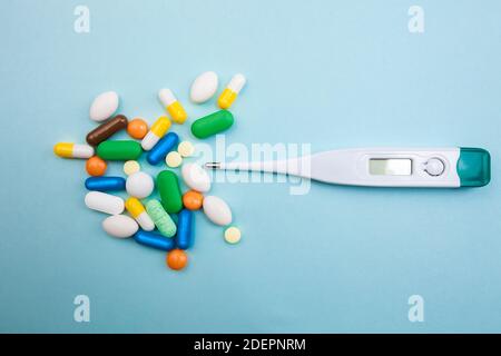 Mehrfarbige Tabletten und Kapseln, ein Thermometer und ein Tonometer auf blauem Hintergrund, Konzept der Behandlung für einen kranken Menschen Stockfoto