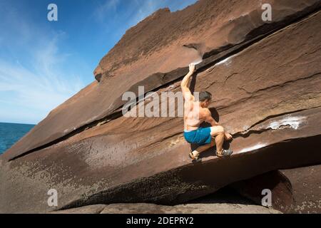 Man klettert an einem sonnigen Tag in St. Bees, Cumbria, Großbritannien, auf Hard Boulder Stockfoto