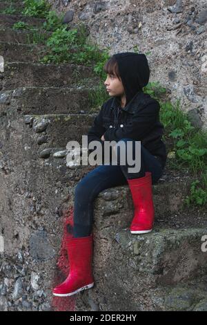 Mädchen in einer schwarzen Jacke, und gekreuzte Arme, sitzen auf einer Leiter im Freien. Stockfoto