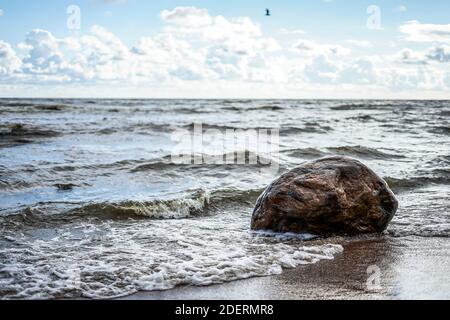 Die Welle schlägt gegen einen großen Stein an der Küste, einen klaren Tag, leichte Wolken Stockfoto