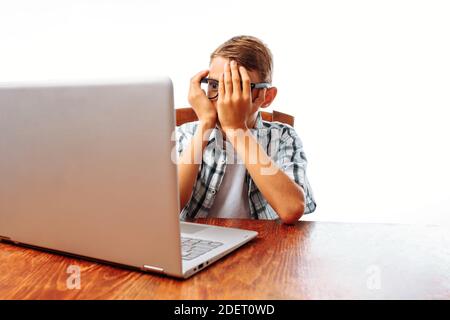 Ein junger Mann sitzt an einem Tisch mit einem Laptop, schockiert von dem, was er sah, Teenager überrascht Blick auf den Laptop, im Studio Stockfoto