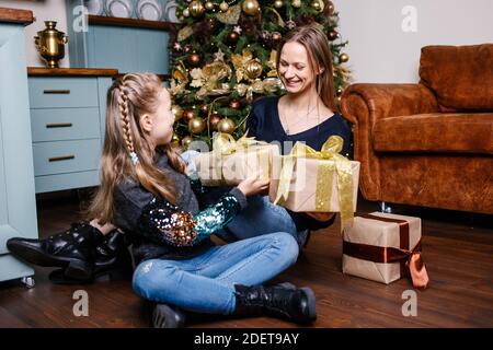 Mutter geht Überraschung für Tochter gibt Geschenk, in der Nähe Weihnachtsbaum zu Hause zu machen. Glücklich lächelndes Mädchen erhält Geschenk von der Mutter. Stockfoto