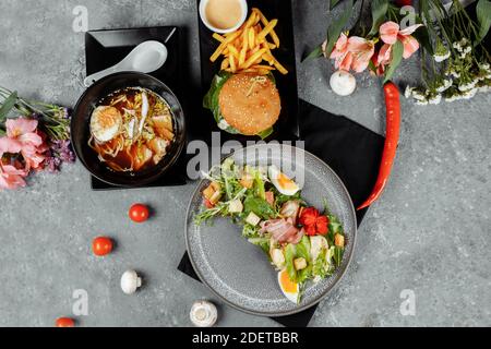 Drei-Gänge-Business Lunch. Mittagessen mit asiatischen Burger Ramen Nudeln und caesar Salat. Stockfoto