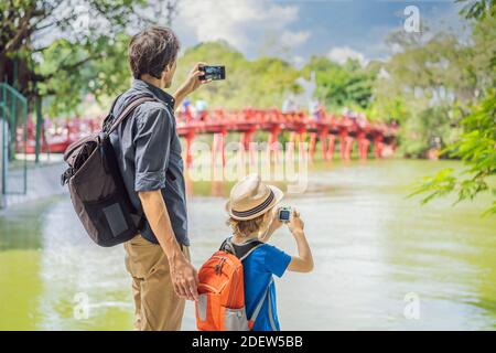 Kaukasischen Vater und Sohn Reisende auf dem Hintergrund der Roten Brücke Im öffentlichen Park Garten mit Bäumen und Reflexion in der Mitten im Hoan Kiem See in Stockfoto