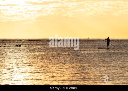 Stand Up Paddler gleitet vor Sonnenuntergang über den flachen Ozean Auf hawaii Stockfoto