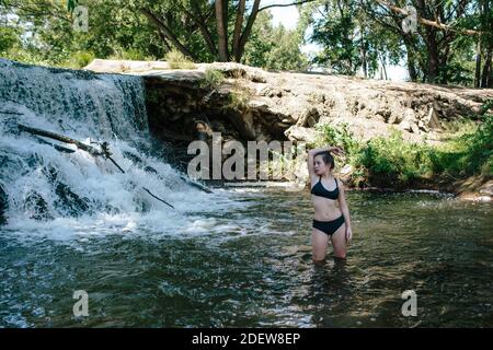 Portrait von teen Mädchen stehen in knietiefen Fluss in der Nähe Ein Wasserfall Stockfoto