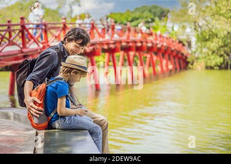 Kaukasischen Vater und Sohn Reisende auf dem Hintergrund der Roten Brücke Im öffentlichen Park Garten mit Bäumen und Reflexion in der Mitten im Hoan Kiem See in Stockfoto