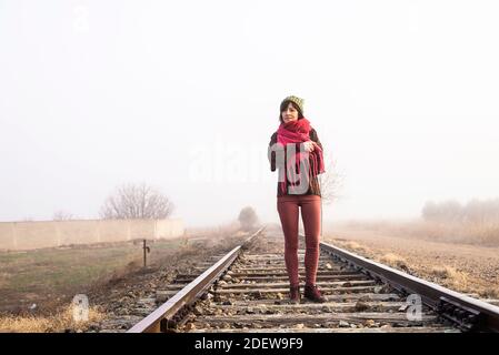 Nachdenkliche Frau, die auf einer nebligen Eisenbahn steht, während sie wegschaut Stockfoto