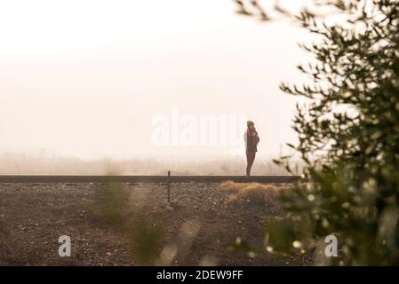 Nachdenkliche Frau, die auf einer nebligen Eisenbahn steht, während sie wegschaut Stockfoto