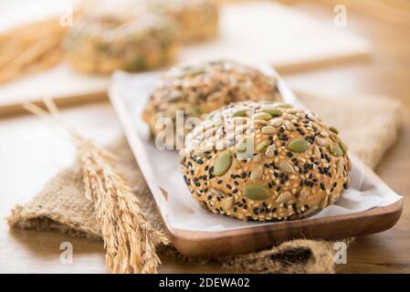Multikorn gemischte Getreidesamen gesunde Brötchen in Holzplatte Anzeige mit auf brauner Jute Sack Textur am Tisch Stockfoto
