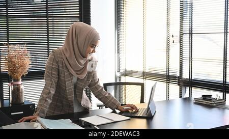 Eine junge arabische Unternehmerin, die einen Hijab trägt, arbeitet online mit einem Laptop im modernen Büro. Stockfoto