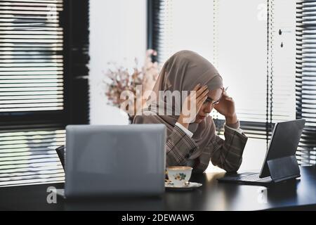 Eine asiatische muslimische Geschäftsfrau fühlt sich überfordert oder deprimiert, während sie im Büro sitzt. Stockfoto