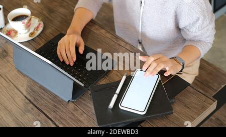 Eine kurze Aufnahme einer Geschäftsfrau, die auf dem Smartphone nach wichtigen Informationen sucht, während sie im Büro ein Tablet verwendet. Stockfoto