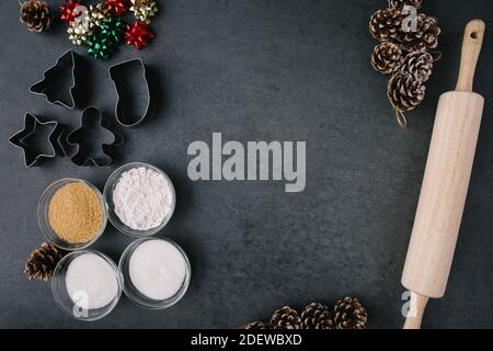 Weihnachtsfeiertage Plätzchen Ausstecher, Weihnachtsdekorationen und Backzutaten auf dunklem Schiefer mit leerem Raum in der Mitte Stockfoto