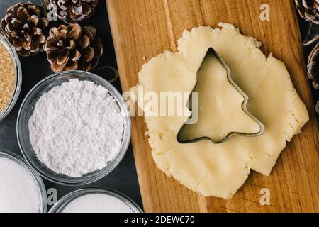 Schneiden Urlaub Weihnachtsbaum Cookie In Roh Cookie Teig Mit Tannenzapfen und Zutaten auf Schiefertanne Stockfoto