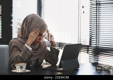 Nachdenkliche oder stressige islamische Frau in Hijab ist Kopfschmerzen und Stress haben ein Problem und Problem ihrer Arbeit. Stockfoto