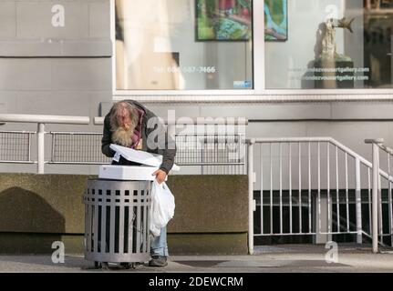 Ein Obdachloser, der in einem Müllcontainer nach Essen sucht. Vancouver, BC, Kanada - November 1,2020. Selektiver Fokus, Straßenbild, Stadtarmut. Stockfoto