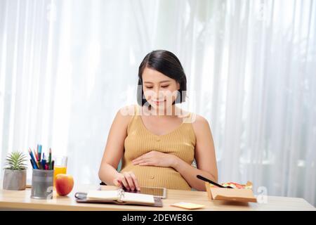 Eine schwangere Frau sitzt an einem Tisch und benutzt einen Tablet-Computer. Stockfoto