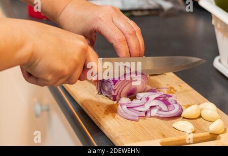 Weibliche Hände schneiden rote Zwiebel auf dem Holzbrett. Nahaufnahme, selektiver Fokus. Stockfoto