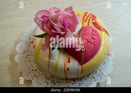 Moderner Mousse-Kuchen mit Spiegelglasur mit essbarem Zucker bedeckt Rose und Schokolade Herz Stockfoto