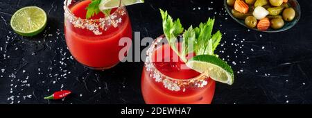 Bloody Mary Cocktail-Panorama mit Limette und Sellerie, mit Gurken und einem heißen Pfeffer, auf dunklem Hintergrund Stockfoto