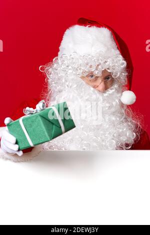 Weihnachtsmann hält grüne Geschenkbox in der Hand, während hinter dem weißen weißen Brett stehen. Stockfoto