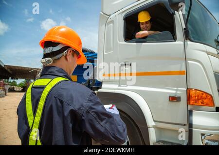 Asiatischer Vorarbeiter mit Sicherheitshüten und Sicherheitsweste trägt ein Auto-Inspektionsdokument auf dem Parkplatz mit LKW-Fahrer, Konzept der Planung Arbeitstag. R Stockfoto