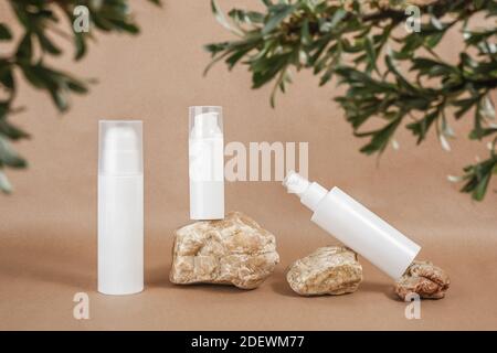 Set von Gesichtspflege Kosmetik. Weiße leere Kosmetikflasche, Tube und Felsen, eingerahmt von grünen Ästen-Blättern, beigefarbener Hintergrund. Natürliches Organisches Spa Cosm Stockfoto