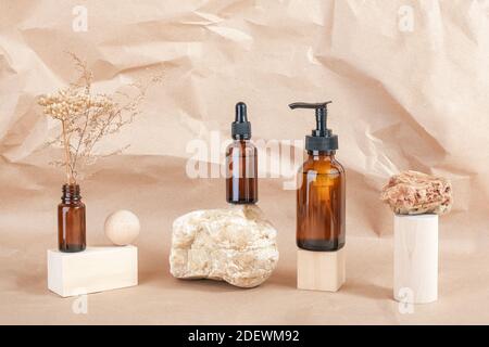 Braune Glasflaschen von Kosmetikprodukten auf Stein, geometrische Holzformen und getrocknete Blumen auf beigem Papierhintergrund. Natürliches organisches Spa Kosmetik B Stockfoto