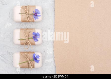 Handgemachte Naturseife Set Grenze mit Bastelpapier, Geißel und blauen Kornblumen auf grauem Stein backgroun dekoriert. Bio-Kosmetik, Null Abfall, Öko Stockfoto