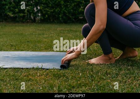 Barfuß weibliche Yoga-Praktizierende Abrollen Matte auf Gras während der Vorbereitung Für Yoga-Unterricht im Hinterhof Stockfoto