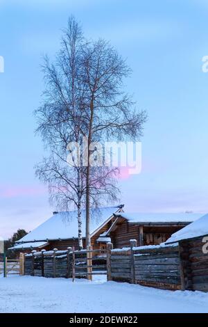 Irkutsk, Russland - 8. Januar 2019: Winterlandschaft mit Holzhäusern Bäume und bunten Himmel während Sonnenuntergang im Museum Taltci. Stockfoto