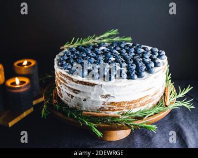 Schokoladenkuchen mit frischen Heidelbeeren verzierten Rosmarinzweig auf einem Holztablett in einem dunklen Innenraum. Stockfoto