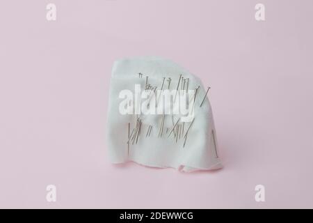 Stück weißes Tuch von einer Vielzahl von Nadeln gekreuzt. Nadelkissen mit Pins auf rosa Hintergrund. Stockfoto