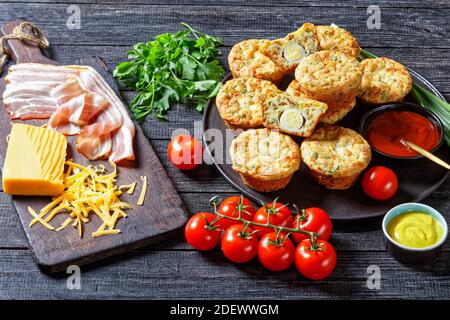 Speck, Ei und Käse Frühstücksmuffins auf einem schwarzen Teller auf einem Holztisch mit Zutaten, horizontale Ansicht von oben Stockfoto