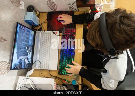 Mit Blick auf einen Jungen saß an einem Schreibtisch, spielte ein Computerspiel auf einem Laptop-Computer mit einer hellen Gaming-Maus und Tastatur. Stockfoto