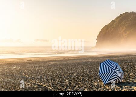 AUCKLAND, NEUSEELAND - 28. Jan 2020: Auckland / Neuseeland - 15 2020. Februar: Blick auf den Sonnenschirm mit weißen und blauen Streifen am Piha-Strand in e Stockfoto