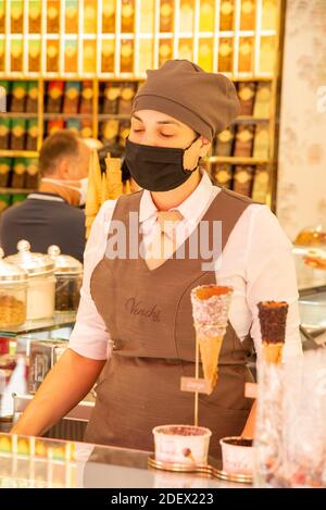 VERONA, ITALIEN - 18. Aug 2020: Eine Eisverkäuferin in einer italienischen Eisdiele mit Schutzmaske vor ihren verschiedenen Eisdielen A Stockfoto