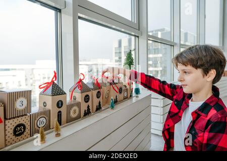 Junge Eröffnung Weihnachten handgemachte Adventskalender in einer Hausform, um die Tage bis Weihnachten im Zimmer Countdown. Stockfoto