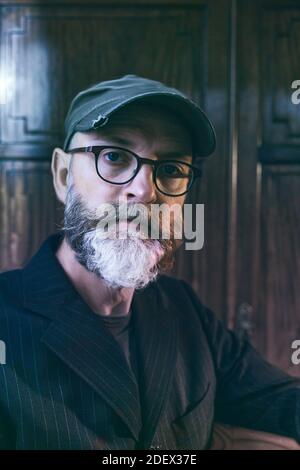 Nahaufnahme Porträt einer männlichen Figur mittleren Alters tragen Brille und eine Kappe mit einem langen Bart Blick auf die Kamera. Stockfoto