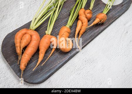 Ein paar der hässlichen Wurzeln von Karotten auf einem hölzernen Schneidbrett. Stockfoto