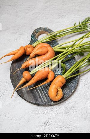 Hässliche Karottenwurzeln liegen auf einem runden Holzschnittbrett. Vertikale Ausrichtung. Stockfoto