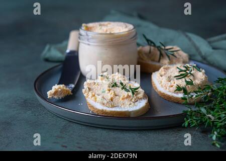 Sandwiches mit geräuchertem Lachs und weicher Frischkäse-Pastete oder Mousse mit Thymian und Rosmarin auf einer Keramikplatte, grüner Betonboden. Selektive Stockfoto