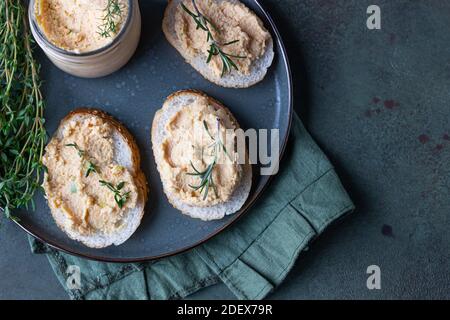 Sandwiches mit geräuchertem Lachs und weicher Frischkäse-Pastete oder Mousse mit Thymian und Rosmarin auf einer Keramikplatte, grüner Betonboden. Selektive Stockfoto