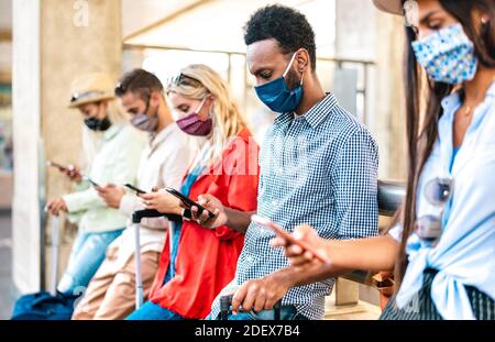 Multirassische Freunde mit Gesichtsmaske mit Tracking-App mit Handy Smartphones - Junge Menschen, die online buchen unter Bahnhof Stockfoto